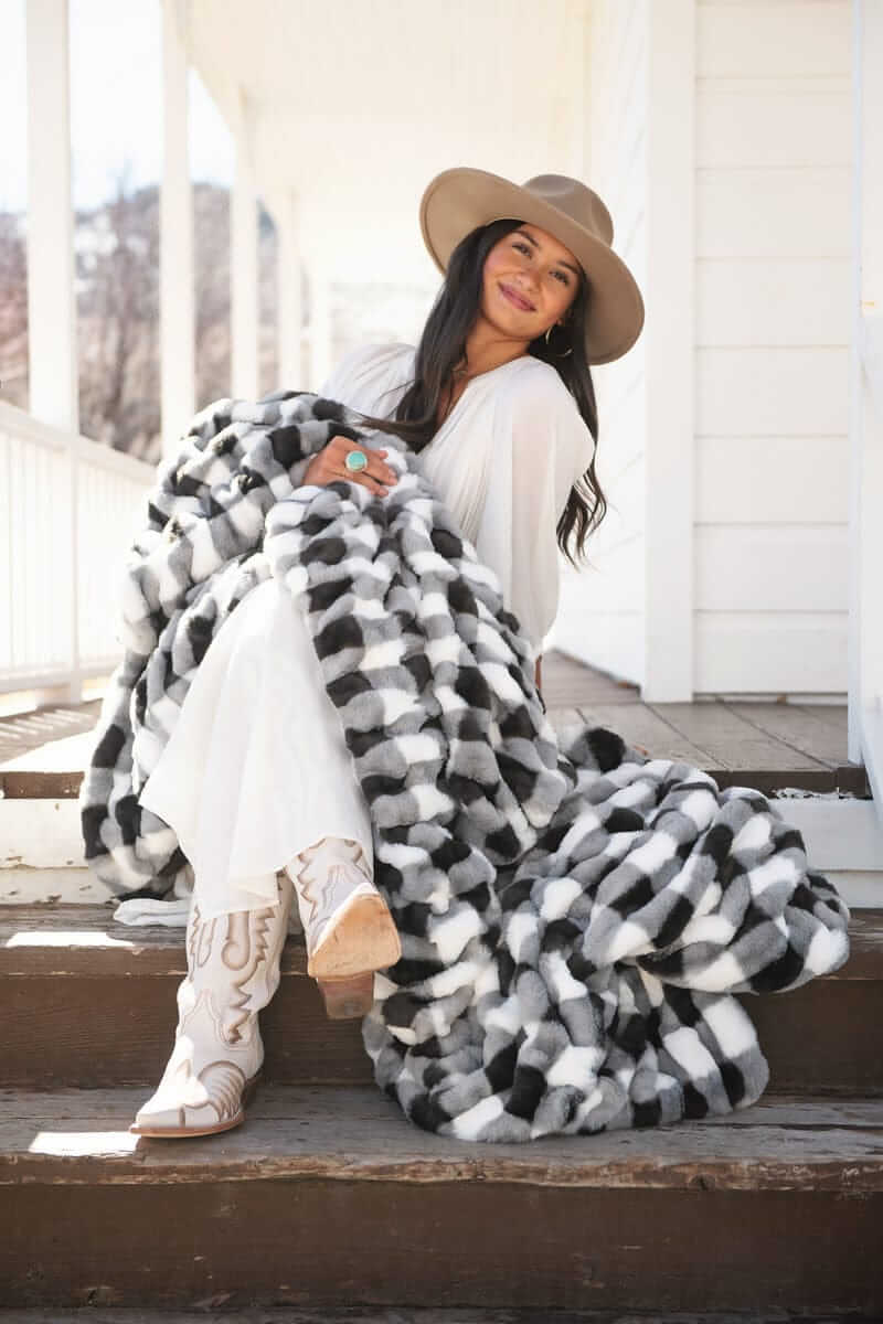 Young woman sitting leaning against a white house with a charcoal gingham check blanket.