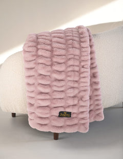 Pink textured blanket draped over a chair with a visible brand label.