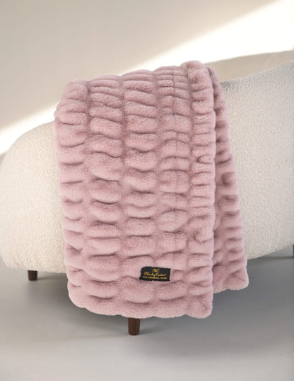 Pink textured blanket draped over a chair with a visible brand label.