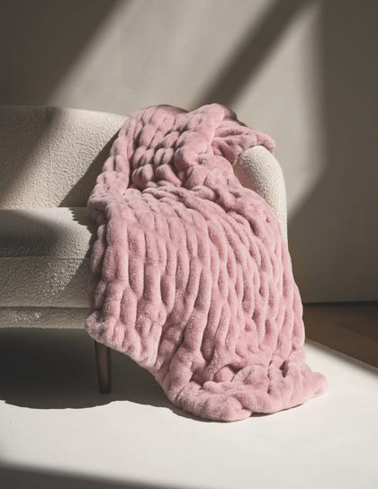 Pink Hugs Heirloom Rose Blanket draped over a beige armchair with soft shadows.
