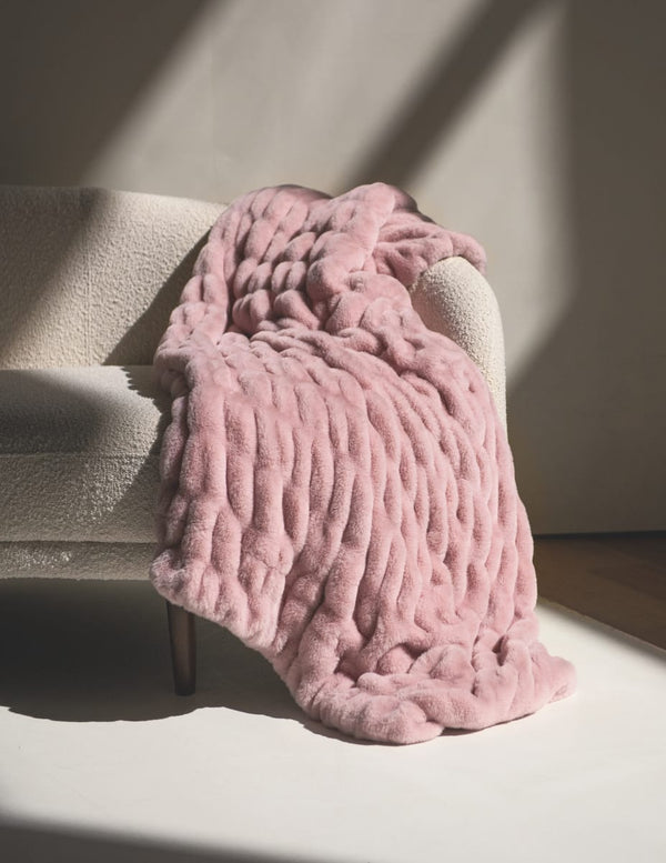 Pink Hugs Heirloom Rose Blanket draped over a beige armchair with soft shadows.