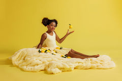 Young girl sitting on a yellow blanket while holding lemons against a yellow background.