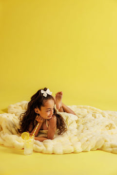Young girl lying on a yellow blanket drinking lemonade, against a yellow background