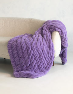 A chunky, thickly textured purple throw blanket draped over a cream-colored armchair against a light gray wall.