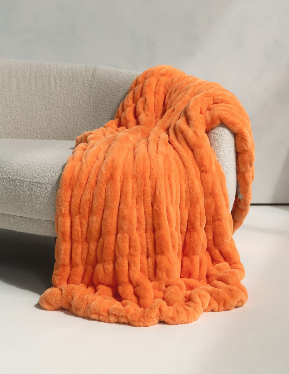 A bright orange blanket draped over a light gray upholstered armchair in a minimalist indoor setting.