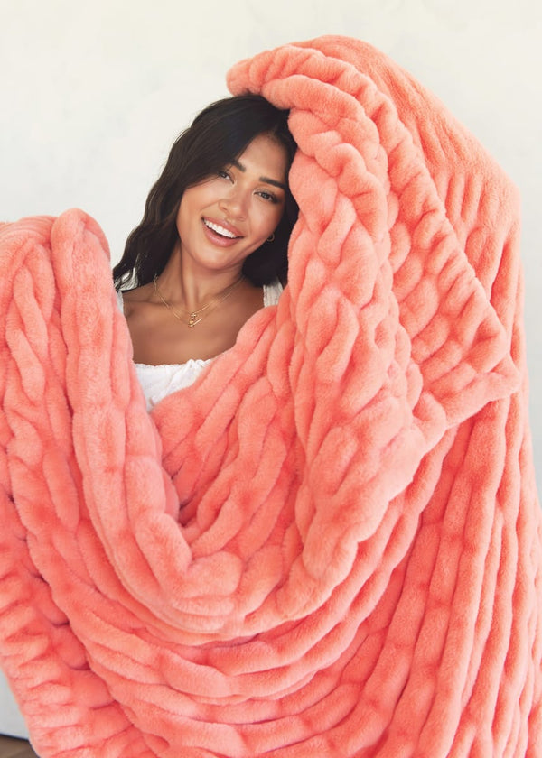 A woman wrapped in a chunky, oversized coral pink plush blanket.