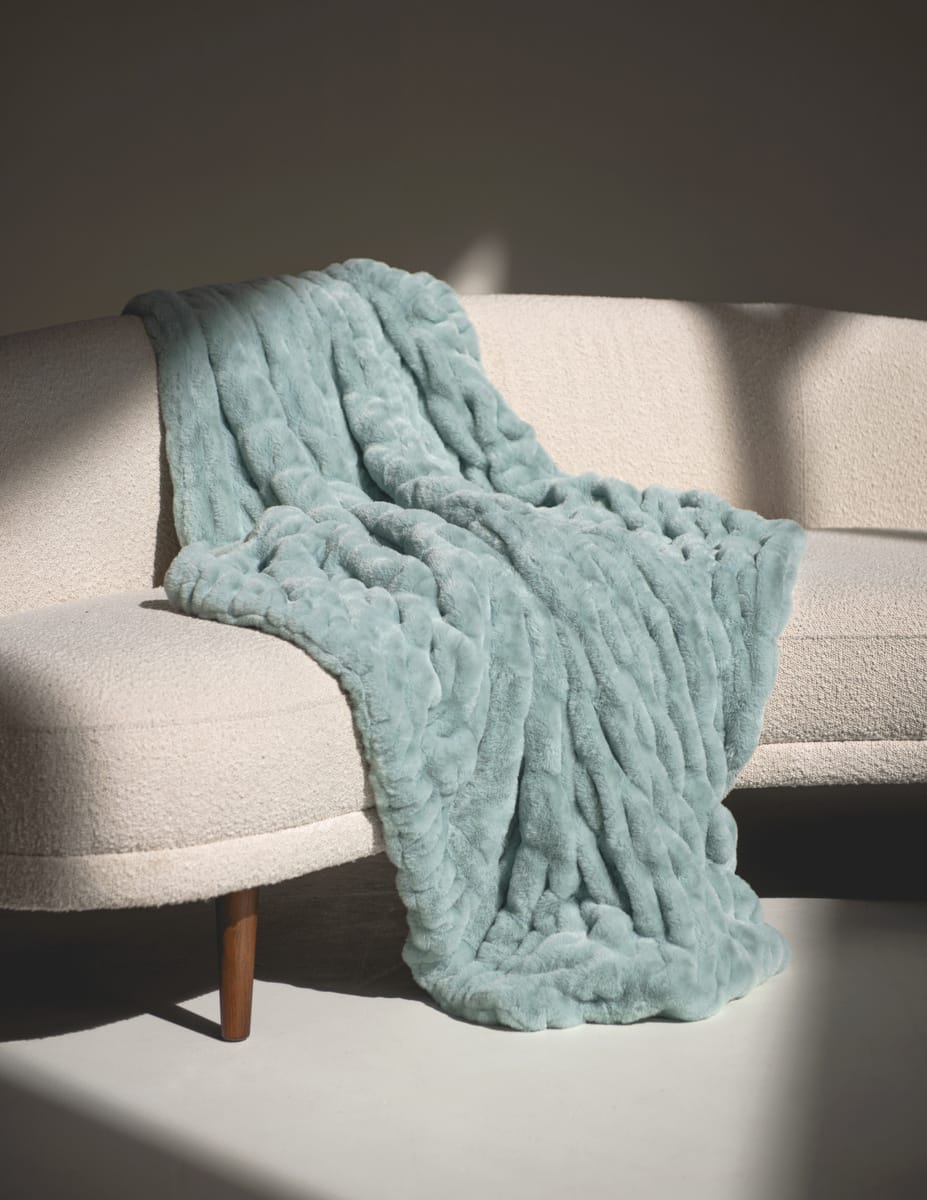 Light blue textured blanket draped over a beige sofa with a neutral background.