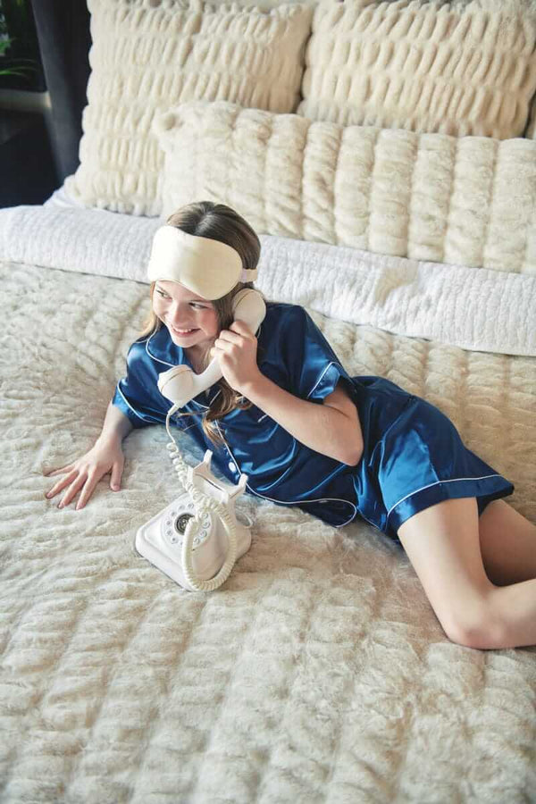 Girl lounging on a bed with plush Minky Couture bedding while using a phone.