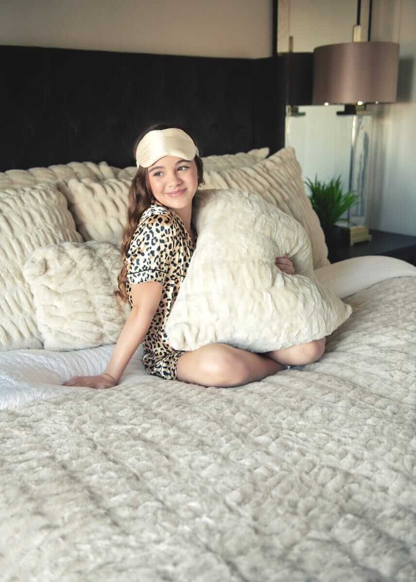 Woman sitting on a bed with white Minky Couture Hugs Ancient Scroll Sham bedding.