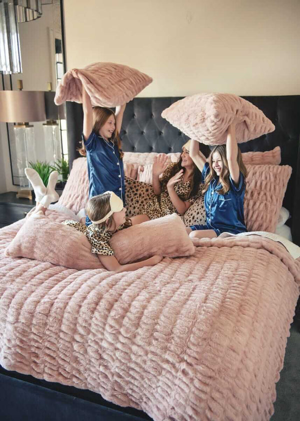 Four girls playing on a bed with plush Minky Couture Hugs Blush Sham bedding and pillows.