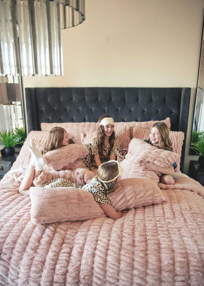 Four girls lounging on a bed with plush Minky Couture Hugs Blush Sham bedding and pillows.