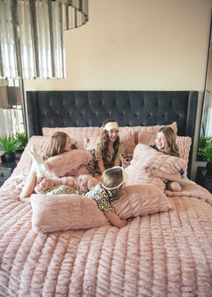 Four girls lounging on a bed with plush Minky Couture Hugs Blush Sham bedding and pillows.