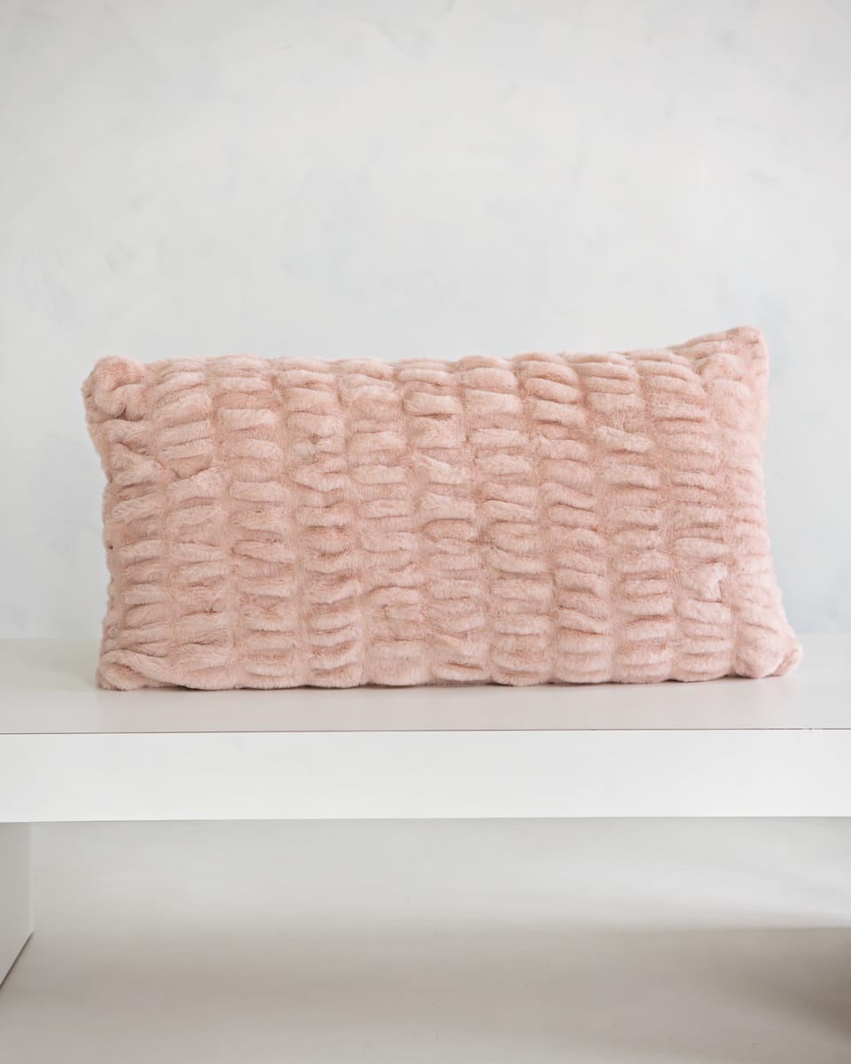 Hugs Blush Sham on a white table, showcasing its soft texture and cozy blush pink color.