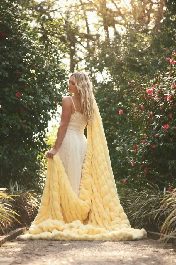 Woman in a white dress holding the Hugs Butter Yellow Blanket in a garden, showcasing its soft and plush texture.