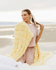 Woman holding a large yellow fluffy blanket in a beach setting