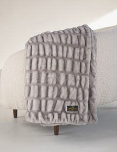Hugs Chai Blanket draped on a cozy chair, showcasing its soft gray texture and stylish design.