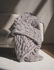 Hugs Chai Blanket draped over a cozy sofa, showcasing its plush texture and soft gray color.