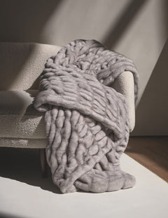 Hugs Chai Blanket draped over a cozy sofa, showcasing its plush texture and soft gray color.