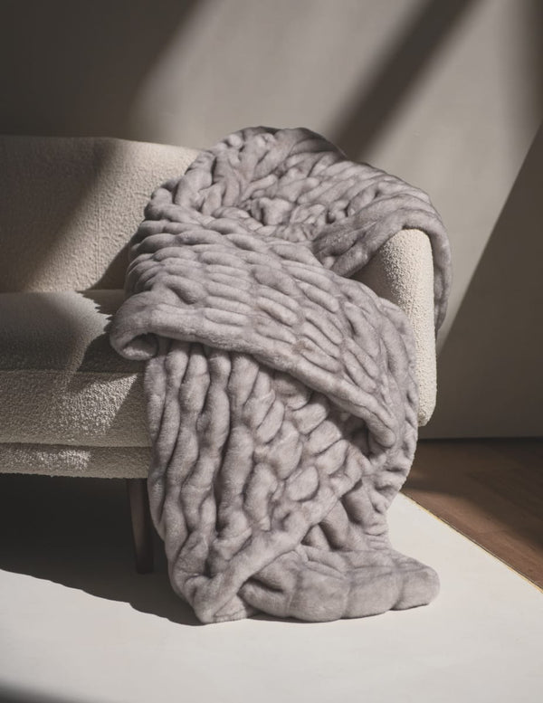 Hugs Chai Blanket draped over a cozy sofa, showcasing its plush texture and soft gray color.