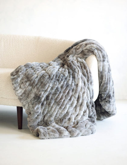 A chunky Minky Couture Hugs Cotton Candy Licorice blanket in shades of gray and white, draped over a cream-colored armchair.