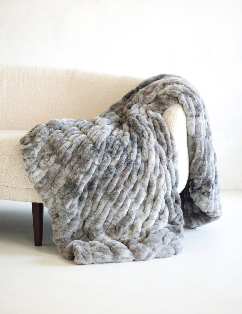A chunky Minky Couture Hugs Cotton Candy Licorice blanket in shades of gray and white, draped over a cream-colored armchair.