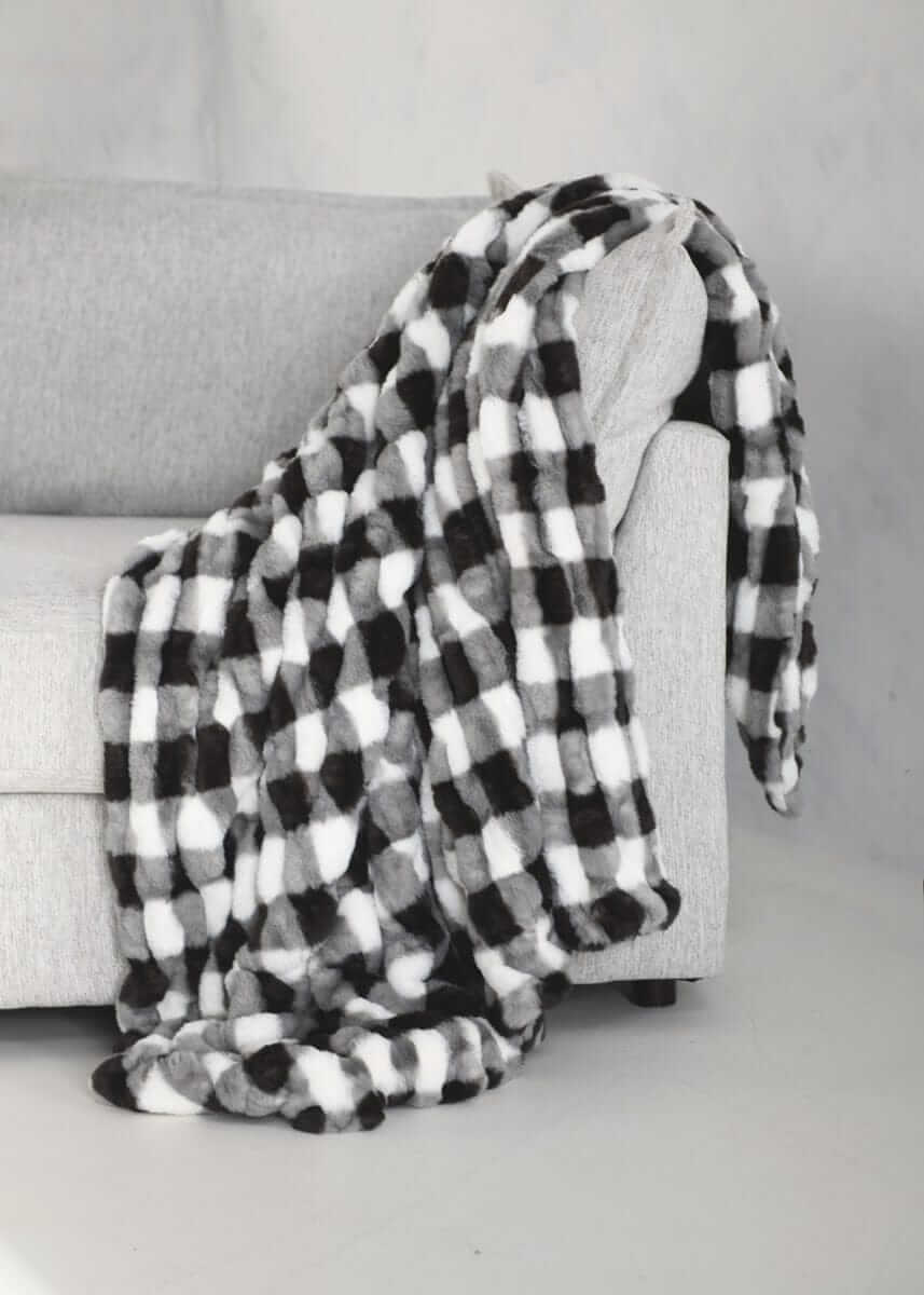 Hugs Gingham Charcoal Blanket draped over a gray couch, featuring a cozy black and white gingham pattern.