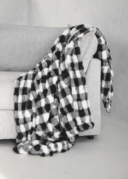 Hugs Gingham Charcoal Blanket draped over a gray couch, featuring a cozy black and white gingham pattern.