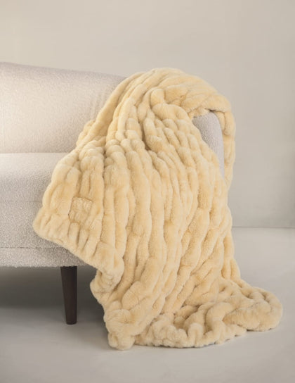 Yellow beige-colored stretchy Hugs Honey Butter Blanket draped over a beige sofa against a neutral background.