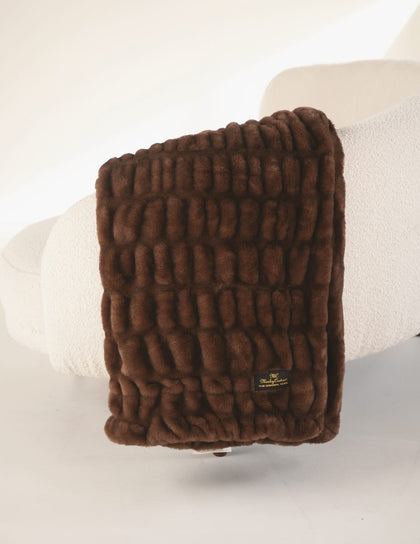 Cozy Hugs Hot Fudge Blanket displayed on a white chair, featuring plush brown texture and stylish design.
