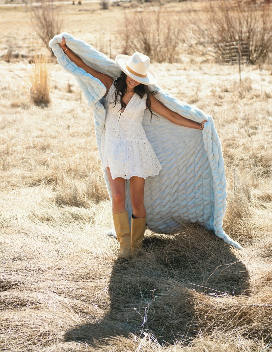 Woman holding the Hugs Ice Blue Blanket, dressed in white, outdoors on a sunny day.