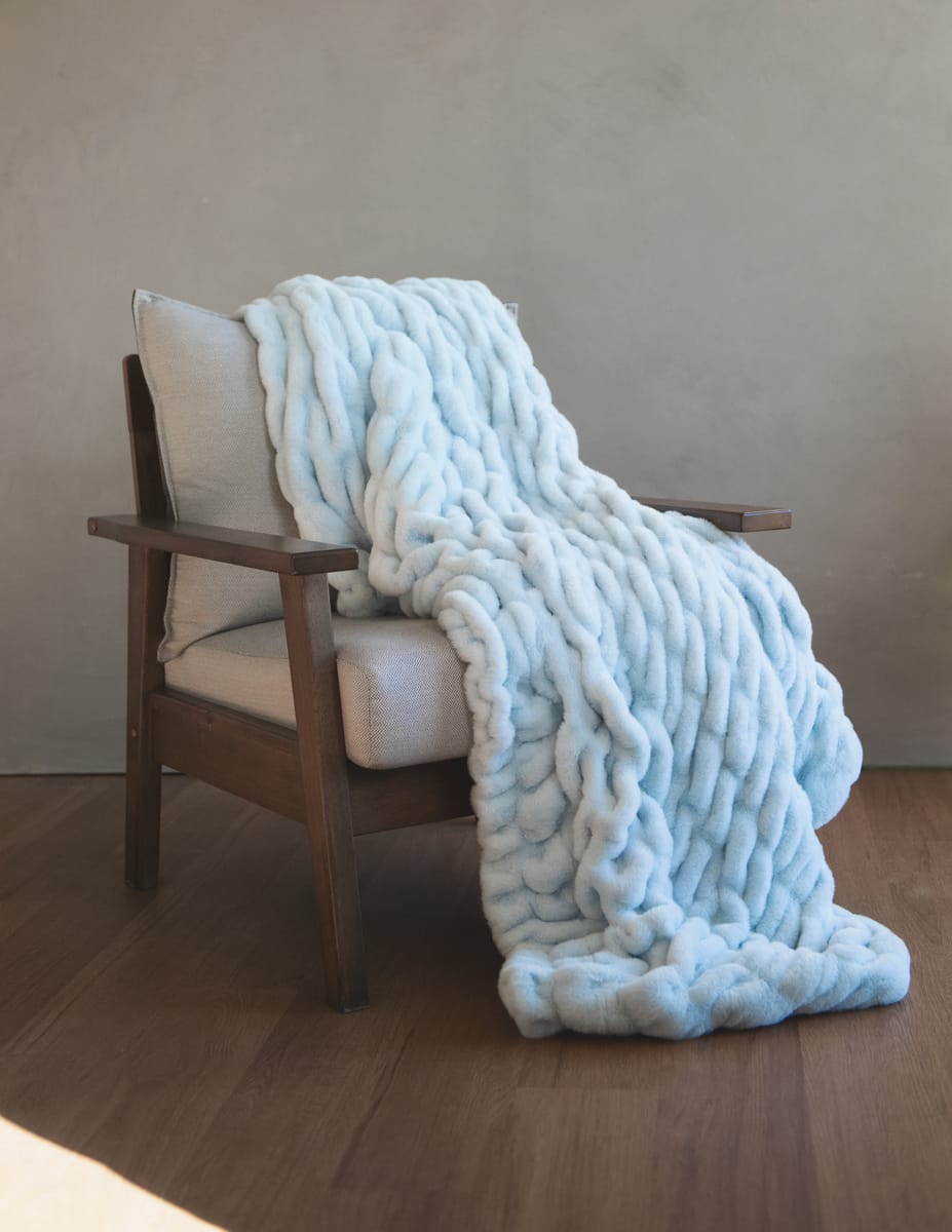 Hugs Ice Blue Blanket draped over a cozy chair, highlighting its ultra-soft, stretchy material and serene color.