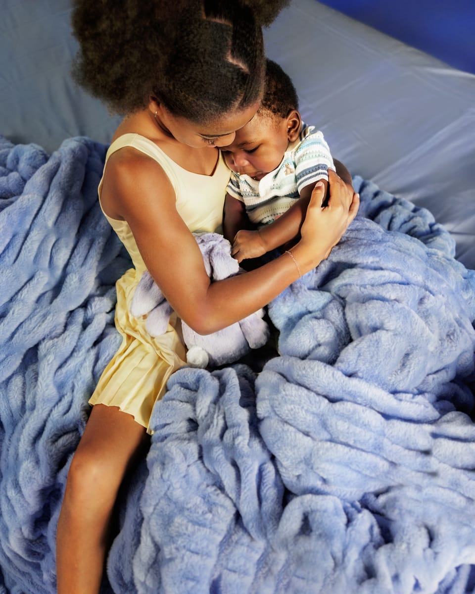 Young girl holding a child under a blue blanket on a bed.