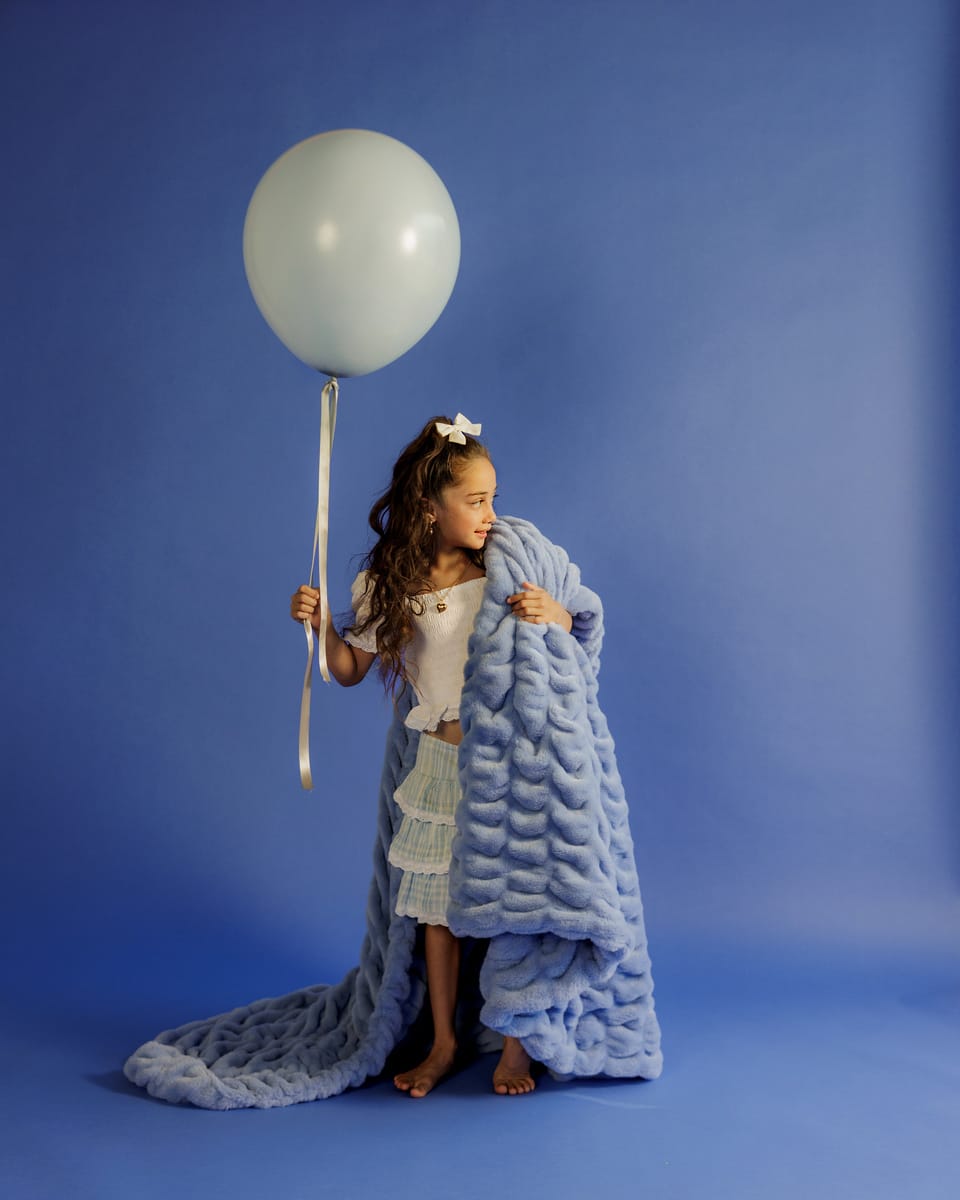 Young girl holding a large white balloon wrapped in a blue textured blanket against a blue background