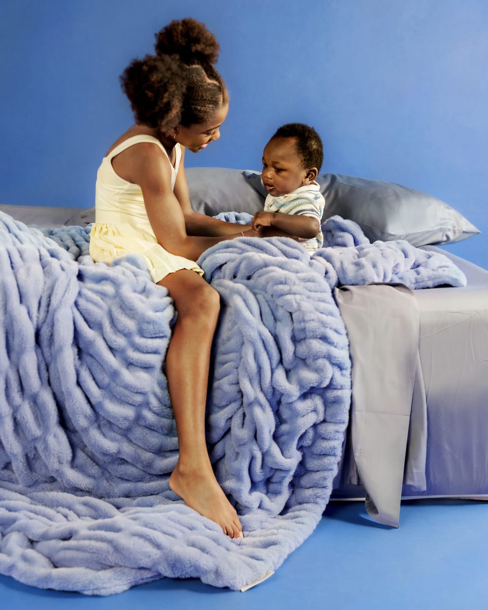 Young girl and child sitting on a bed with a blue blanket
