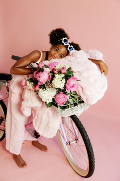 Young girl with a bicycle and flower basket with a light pink blanket on a pink background