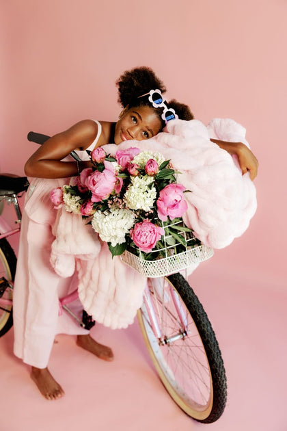 Young girl with a bicycle and flower basket with a light pink blanket on a pink background