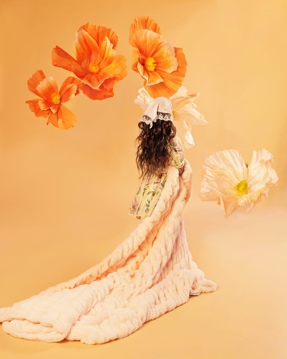 Young girl holding a pastel orange blanket in a flowing dress with large orange flowers on an orange background