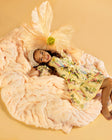 Young girl lying on a large, fluffy pastel orange blanket with a yellow dress against a beige background