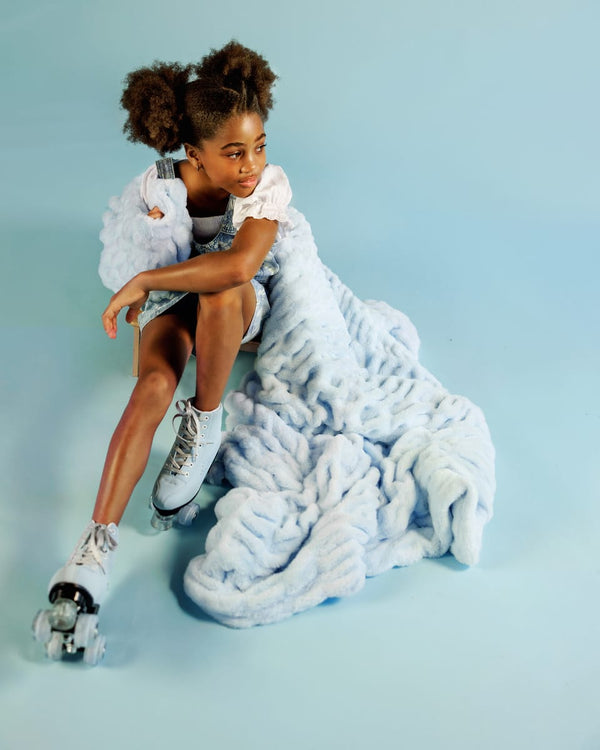 Young girl sitting with a light blue blanket against a light blue background.