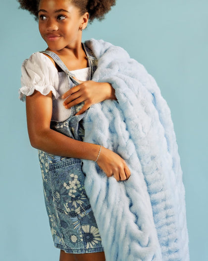 Young girl holding a light blue blanket against a light blue background