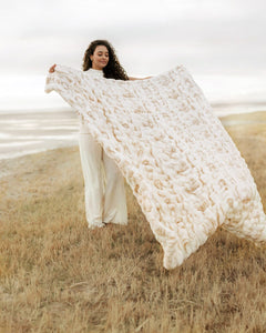 Woman holding a large white textured Hugs Marble Sand Blanket in an open field.