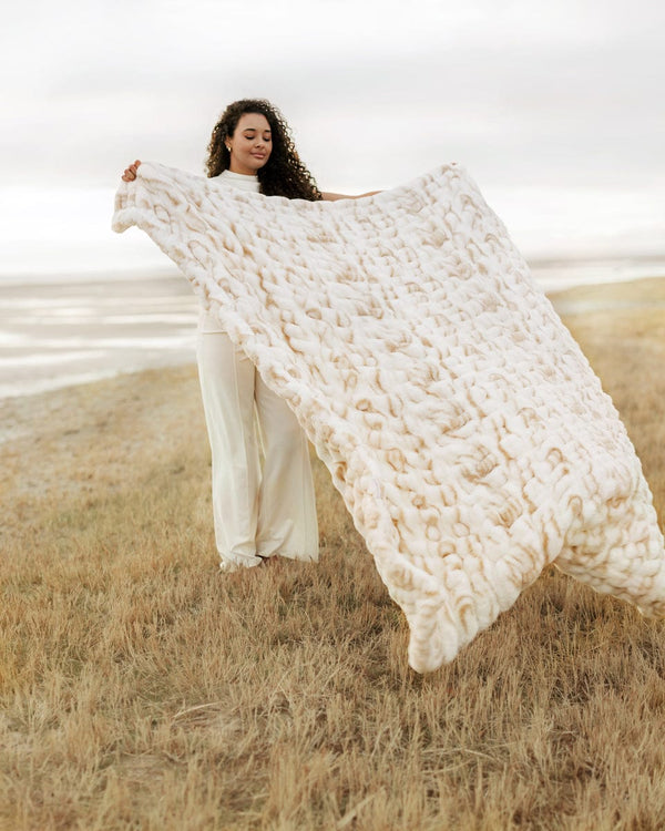 Woman holding a large white textured Hugs Marble Sand Blanket in an open field.