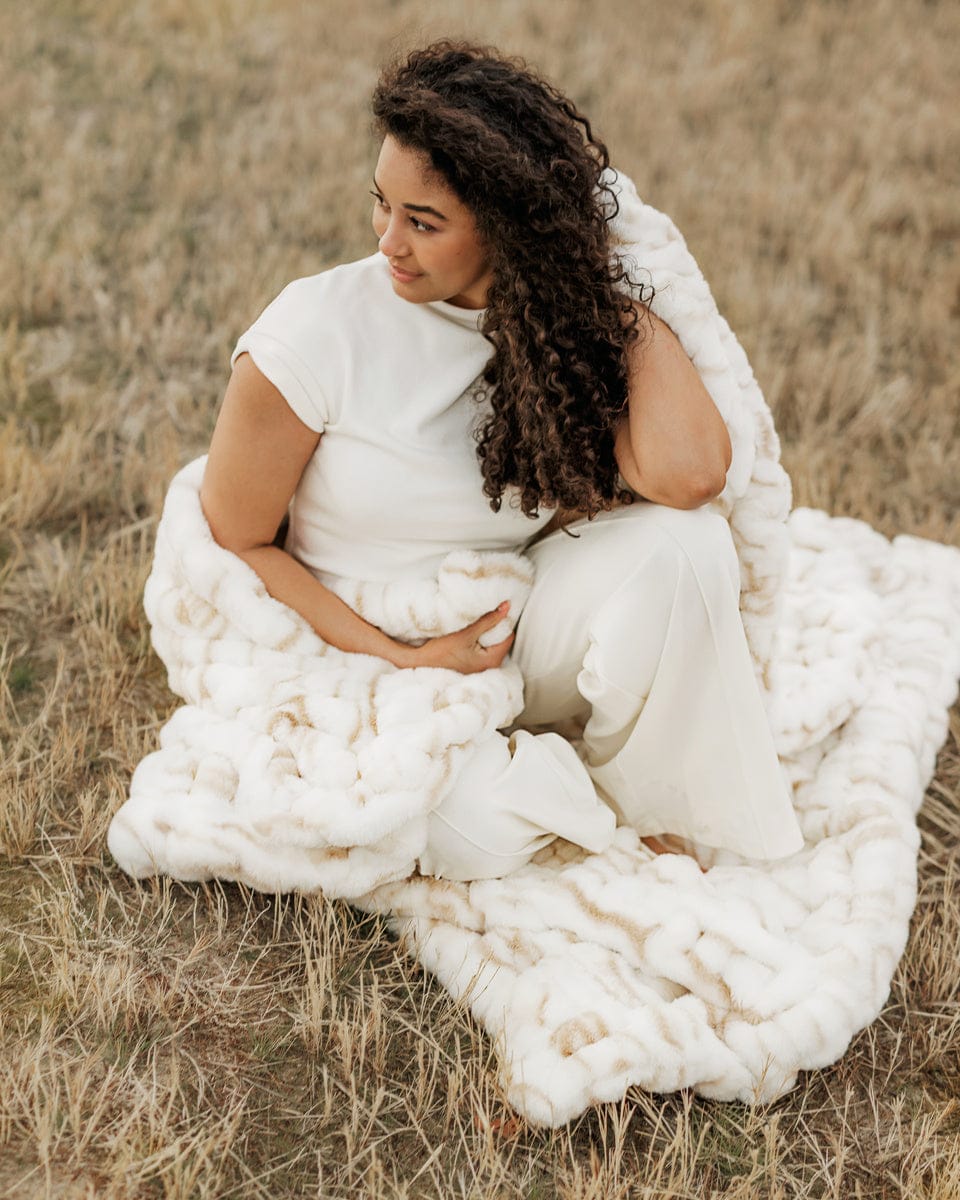 Woman wrapped in a Hugs Marble Sand Blanket sitting in a field.