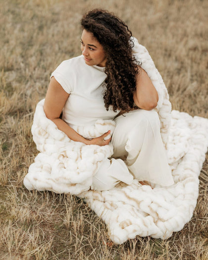 Woman wrapped in a Hugs Marble Sand Blanket sitting in a field.