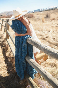 A woman wrapped in the Hugs Midnight Blue Blanket, enjoying cozy warmth outdoors by a wooden fence.