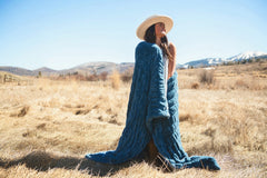 Woman wearing the Hugs Midnight Blue Blanket outdoors, showcasing its cozy material in a picturesque landscape.