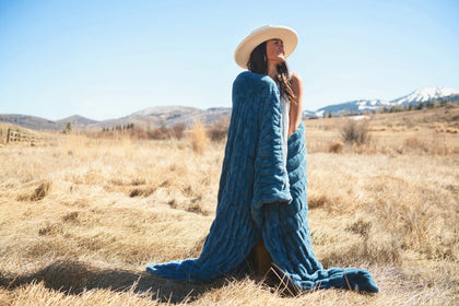 Woman wearing the Hugs Midnight Blue Blanket outdoors, showcasing its cozy material in a picturesque landscape.