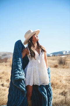Woman in a white dress holding the Hugs Midnight Blue Blanket outdoors against a clear sky.