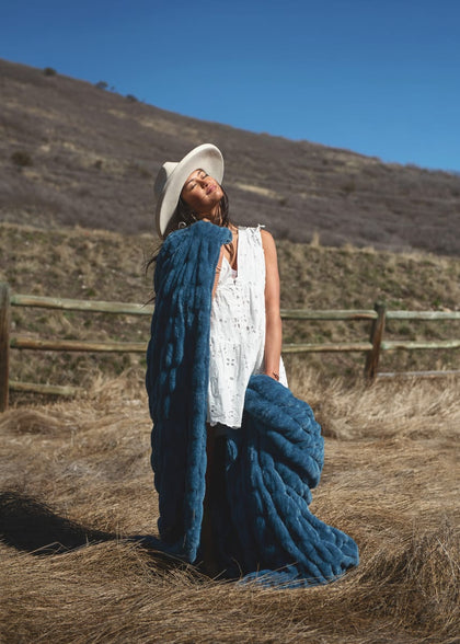 Woman enjoying the Hugs Midnight Blue Blanket outdoors with a hat on a sunny day.