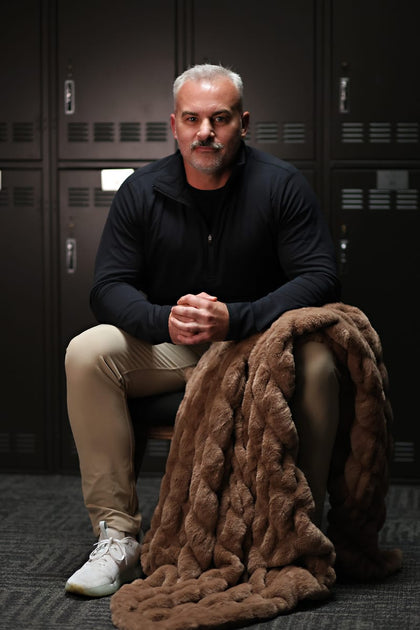 Man sitting on the floor with a Minky Couture Hugs Milk Chocolate blanket in front of lockers